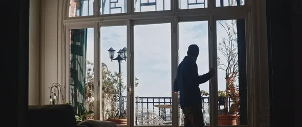 Man walking towards balcony window and grabs his coffee