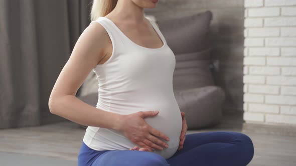 Woman Expecting a Baby Holds Her Hands on Her Stomach Meditates on the Floor of the House Enjoying