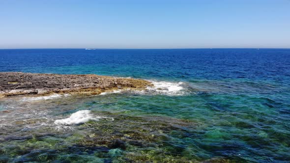 Aerial forward view of waves splashing rocky limestone emerald blue beach in  Sliema, Malta