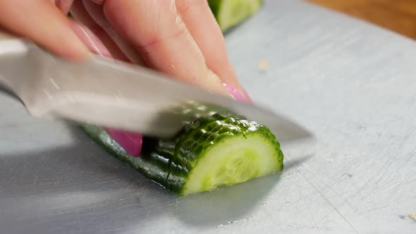 Female slicing fresh cucumber in half on plastic board, close up view