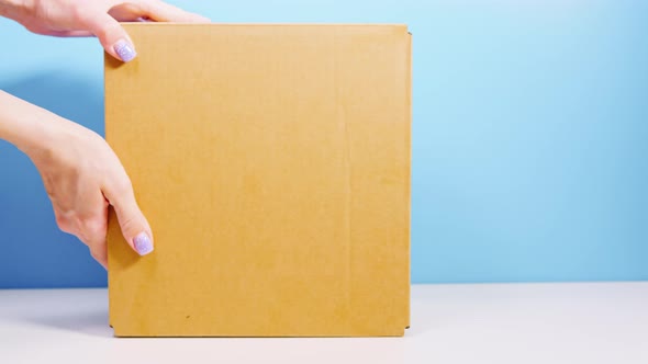 Women's Hands Pass a Cardboard Box Off the White Table to a Man