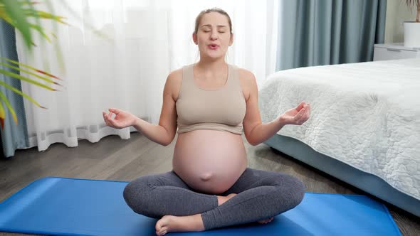 Zoom Out Shot of Happy Smiling Pregnant Woman Sitting on Fitness Mat at Home and Meditating