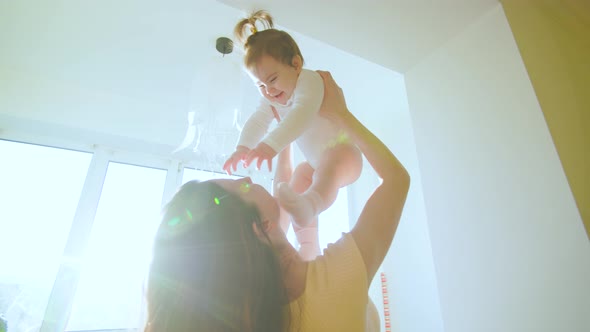 Caucasian Mom is Lifting Her Toddler Baby Girl High Up and Playing in the Sunlight at Home