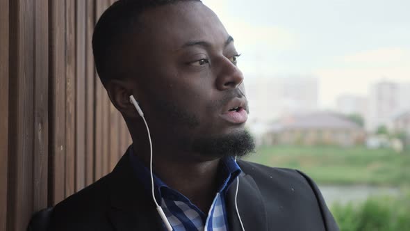 Black Man in Earphones is Listening Music at City Street During Rain