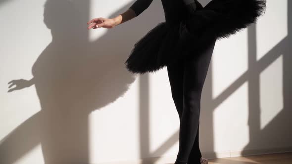 Ballerina in Black Tutu Gracefully Dances Against White Wall in Bright Sunlight