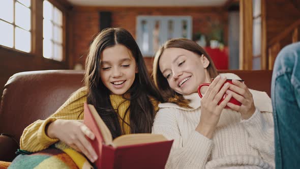 Preteen Daughter Reading Book to Her Young Mom Who Laughing Talking Listening and Drinking Tea While