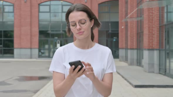 Young Woman Browsing Internet on Smartphone while Walking on Street