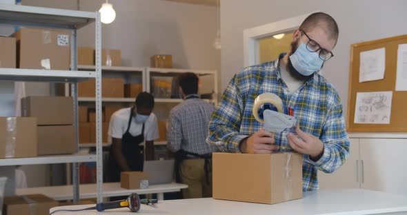 Warehouse Worker Man in Mask Packing Cardboard Box with Sticky Tape