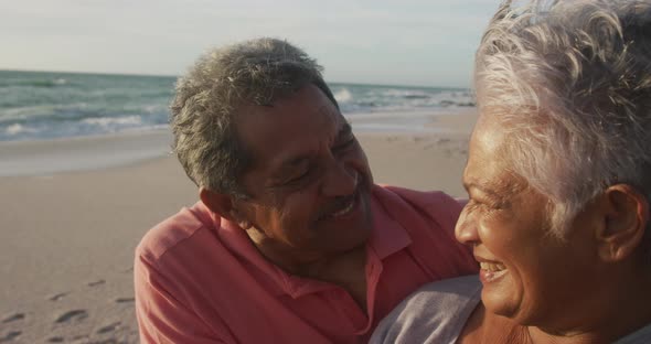 Portrait of happy hispanic senior couple laughing and embracing on beach at sunset