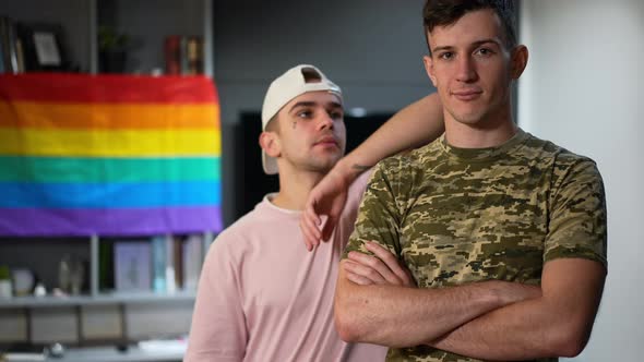 Young Gay Man in Military Uniform Posing Indoors with Excited Boyfriend Bragging Engagement Ring