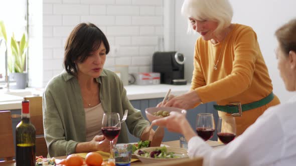 Handsome blond mature woman putting salad on her girlfriends plates