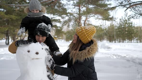 Young Family Mom Son and Dad are Building a Snowman in Winter City Park