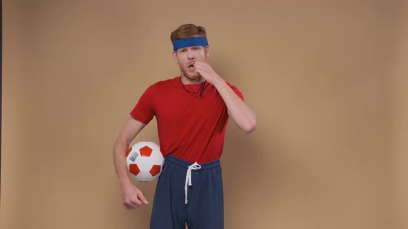 Funny Coach with Soccer Ball Blowing Whistle on a Beige Background