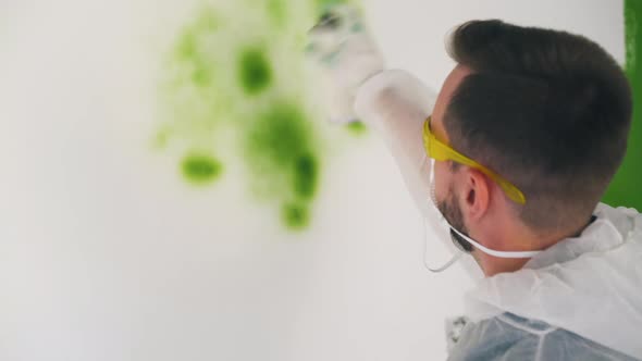 Man in Workwear Paints Wall Using Green Spray in Room