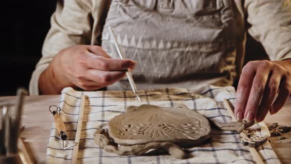 Young Woman Potter Makes Patterns on the Wet Clay Plate Using a Tool