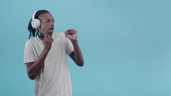 Black Man Listens to Music with Headphones and Holding a Phone in Hand Emotionally Dancing Smiling