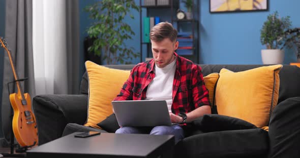 Smiling Millennial Boy Sit Relax on Couch Using Modern Laptop Browsing Unlimited Wireless Internet alt