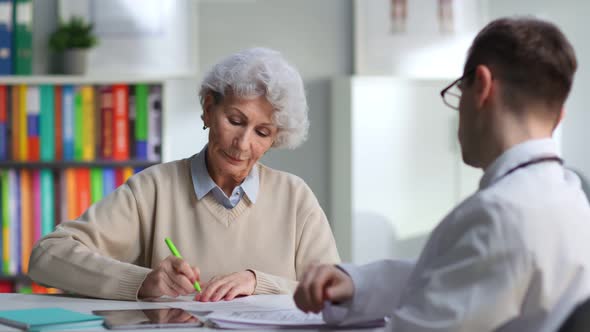 Elderly Female Patient Sign Medical Service Contract in Doctor Office