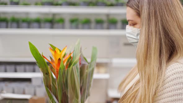 a Young Woman in a Protective Mask Chooses an Exotic Flower in a Store Among Other Flowers
