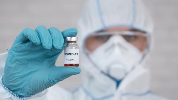 Doctor Holding Covid19 Vaccine Bottle Indoors Wearing Protective Hazmat Suit