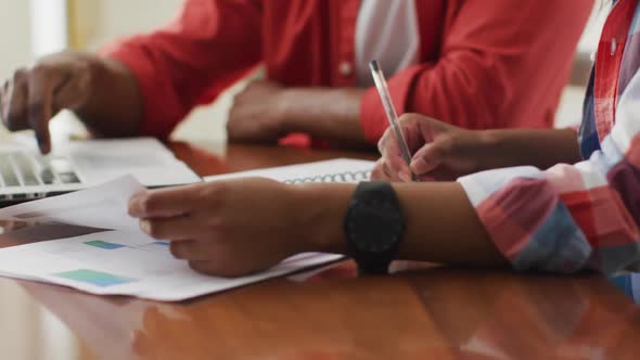 Hands of biracial couple sitting at table with laptop and counting home budget