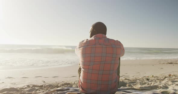 Senior african american man wearing shirt and sitting on sunny beach