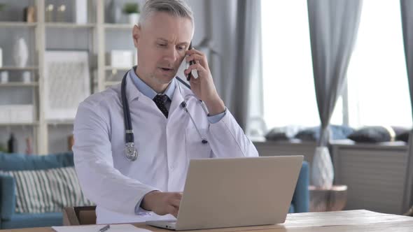 Doctor Working on Laptop and Talking on Phone with Patient