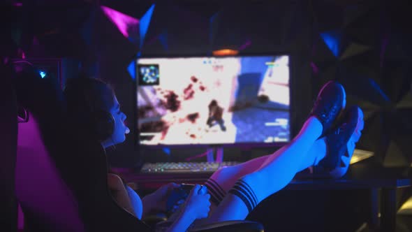 Young Attractive Woman Playing Games in Gaming Club with Her Legs on the Table and Chewing a Bubble