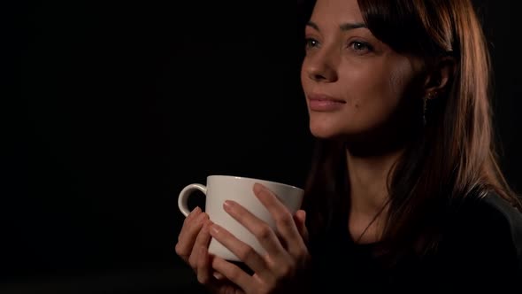 Sexual and Seductive Young Woman Is Smiling Sitting in Black Background, Holding Tea Cup in Hands