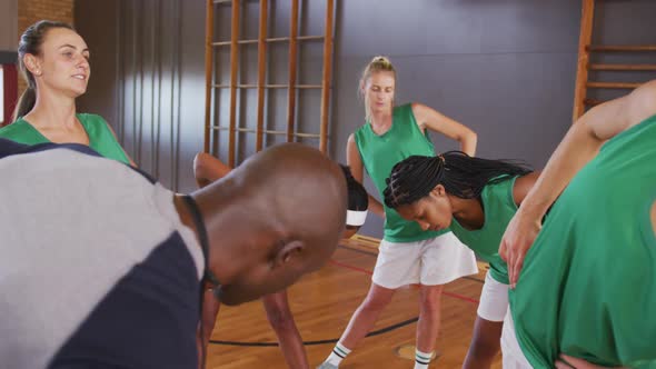 Diverse female basketball team stretching with male coach