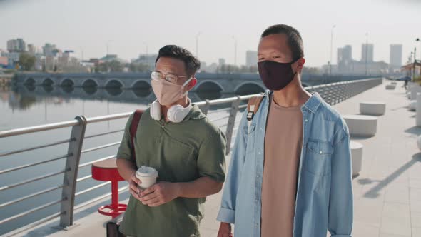 Two Asian Men in Face Masks Walking along Embankment