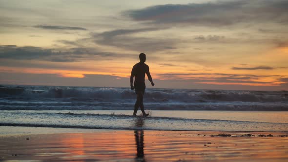 Silhouette of Muscular Man with a Naked Torso Walking on the Beach at Sunset.