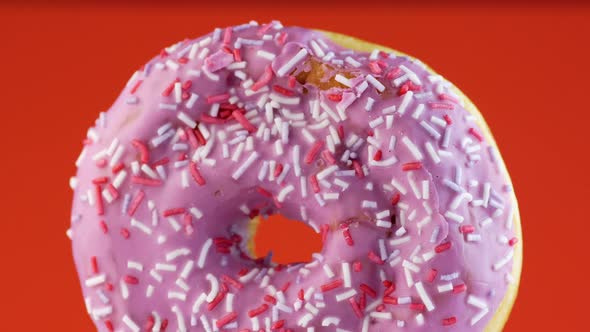 Close-up of a delicious round donut covered with sweet icing rotates on a bright orange background.