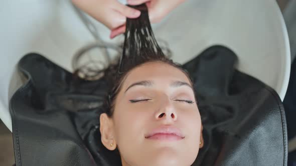 Asian young woman lying down on salon washing bed getting hair washed in hair salon by stylist.