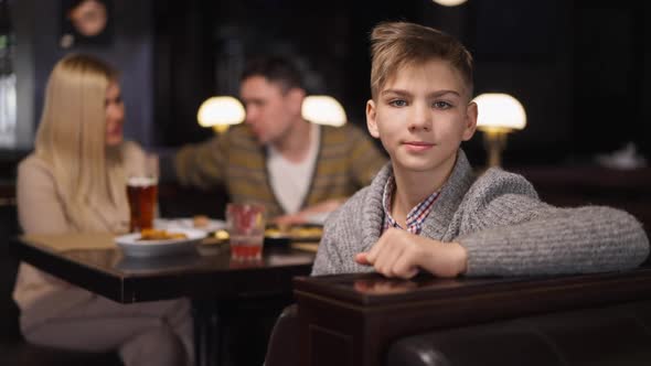 Happy Boy Gesturing Thumb Up Smiling Looking at Camera Sitting with Couple of Parents in Restaurant