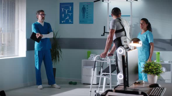 Doctors Discussing Rehabilitation Progress of Man Strolling with Walking Frame