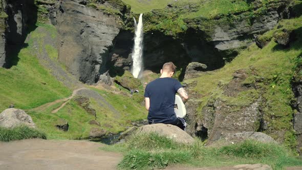 Man playing guitar in front of a beautiful waterfall in Iceland. SlowMo and real time shots from the