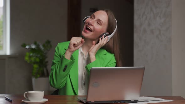 Cheerful Woman Listens to Music in Headphones at Workplace