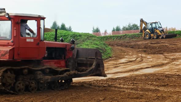 Crawler Tractor Bulldozer with a Metal Bucket Rides on a Dirt Road to Excavator