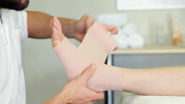 Physiotherapist putting bandage on injured feet of patient