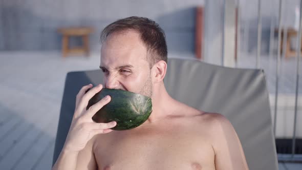 Happy Bearded Man Enjoys Eating Watermelon Sitting Shirtless in Deckchair on Vacation  Face Closeup