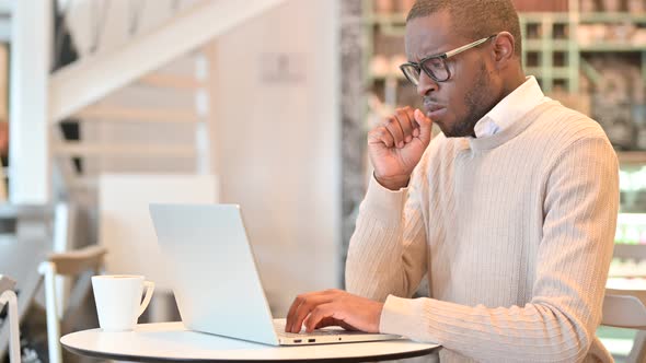 Sick African Man with Laptop Coughing in Cafe