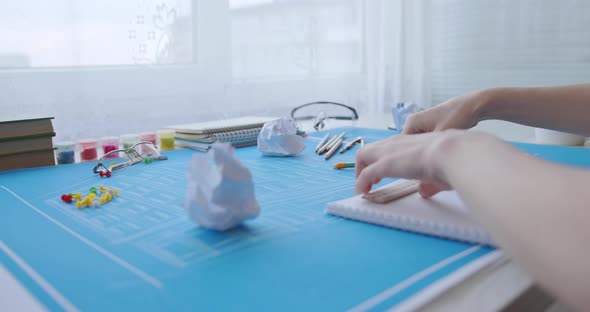 A young woman works and studies architecture from blueprints. She draws with a pencil in a notebook