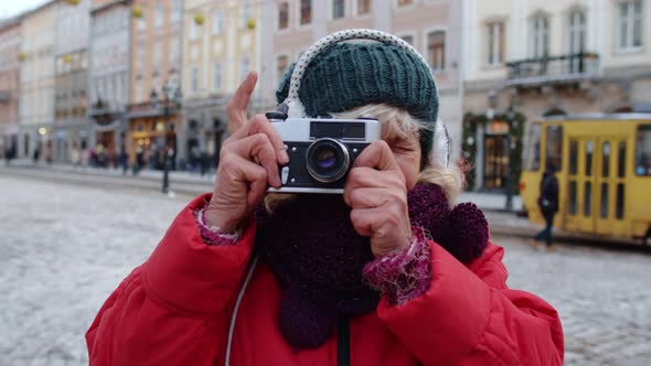 Senior Old Woman Tourist Taking Pictures with Photo Camera Using Retro Device in Winter City Center