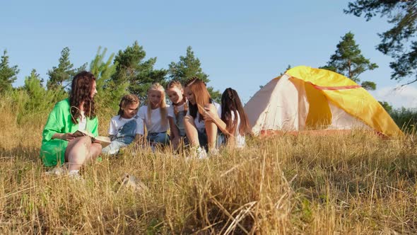 Group of children sitting on grass in forest with they teacher.