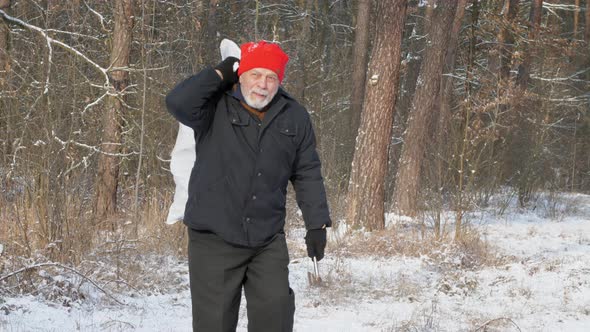 Aged Man Walks Along Snowy Road Holding Axe and Bag