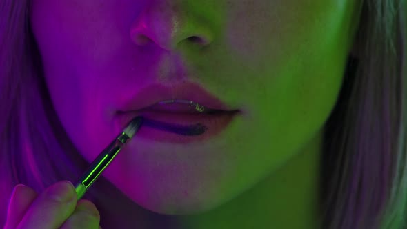 Attractive Female Lips and Mouth. Young Woman Paints Her Lips with a Lipstick Brush. Close Up Macro