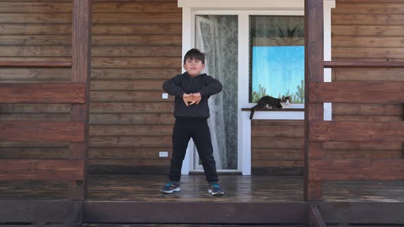 A Little Boy is Playing Sports on the Terrace Against the Background of a Beautiful House A Cat is