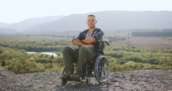 Guy-Invalid in Wheelchair Poses on Camera with Crossed Arms on the Mount 