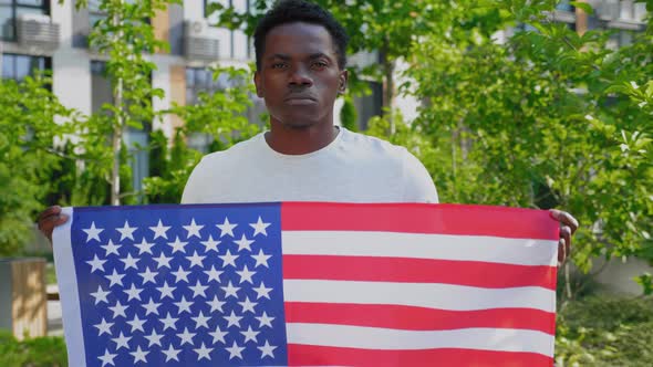 Portrait Afroamerican Man Holding an American Flag and Looks Camera in Summer